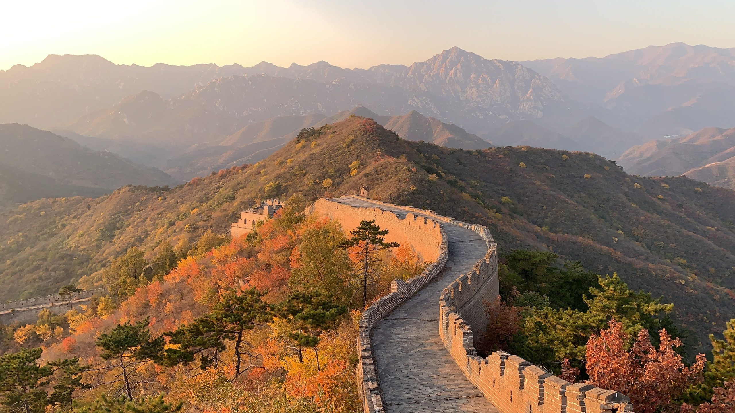 Great Wall of China going through hill with green trees with mountains behind on sunny day
